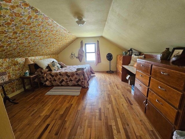 bedroom with a textured ceiling, wood-type flooring, and vaulted ceiling