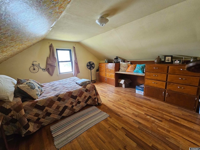 bedroom with a textured ceiling, wood-type flooring, and lofted ceiling