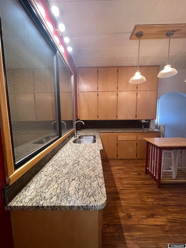 kitchen with sink, dark hardwood / wood-style flooring, pendant lighting, and light stone countertops