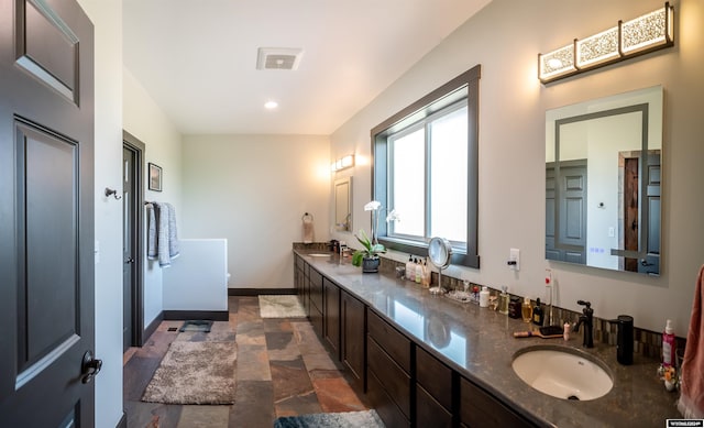 full bath featuring visible vents, a sink, stone finish flooring, double vanity, and baseboards