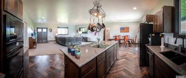 kitchen featuring black appliances, a center island with sink, a sink, recessed lighting, and dark brown cabinets