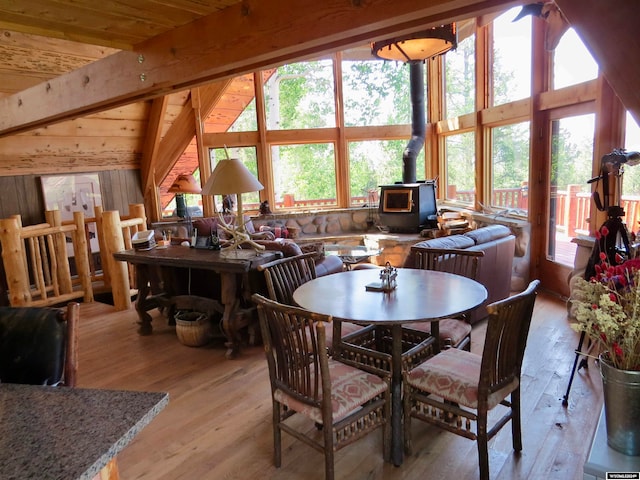 dining room featuring light hardwood / wood-style floors, a wood stove, wooden ceiling, and vaulted ceiling with beams