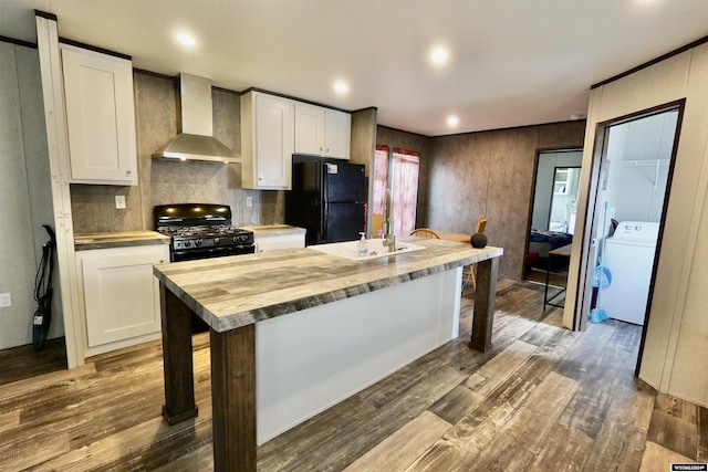 kitchen with washer / clothes dryer, white cabinetry, a kitchen island with sink, black appliances, and wall chimney range hood