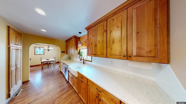 kitchen featuring stainless steel dishwasher, sink, decorative light fixtures, dark hardwood / wood-style flooring, and light stone counters