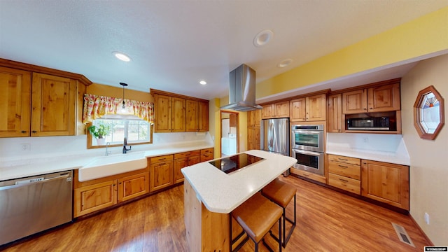 kitchen with a center island, island exhaust hood, stainless steel appliances, sink, and hanging light fixtures