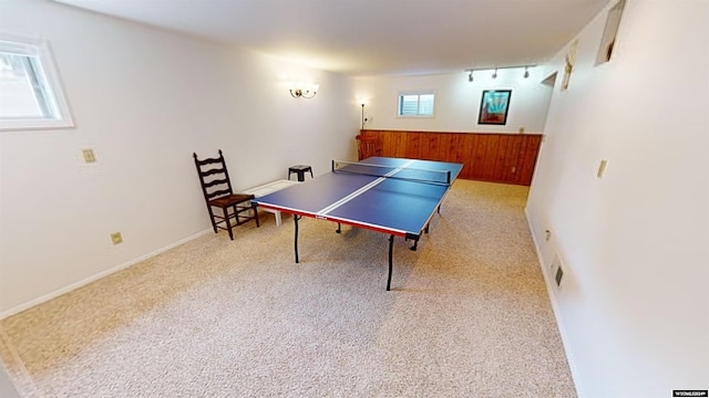 recreation room featuring rail lighting, a wealth of natural light, wooden walls, and light colored carpet