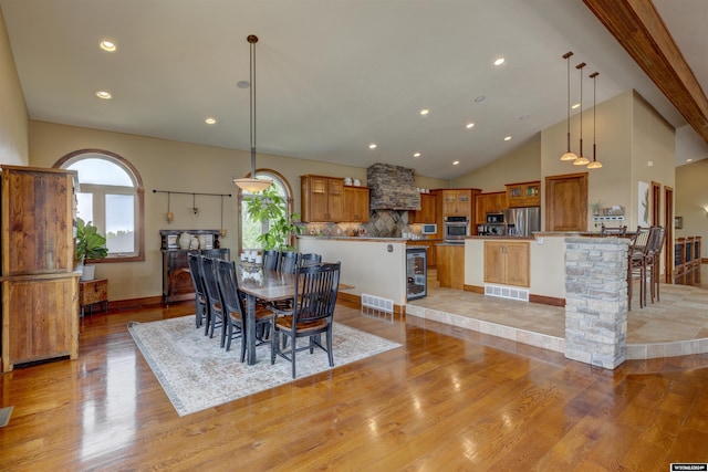 dining space featuring high vaulted ceiling, beverage cooler, visible vents, and light wood-style flooring