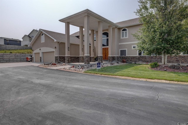 greek revival inspired property featuring a garage, stone siding, a front yard, and stucco siding