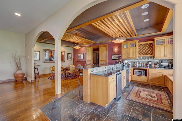 kitchen with a peninsula, light brown cabinetry, stainless steel microwave, and glass insert cabinets