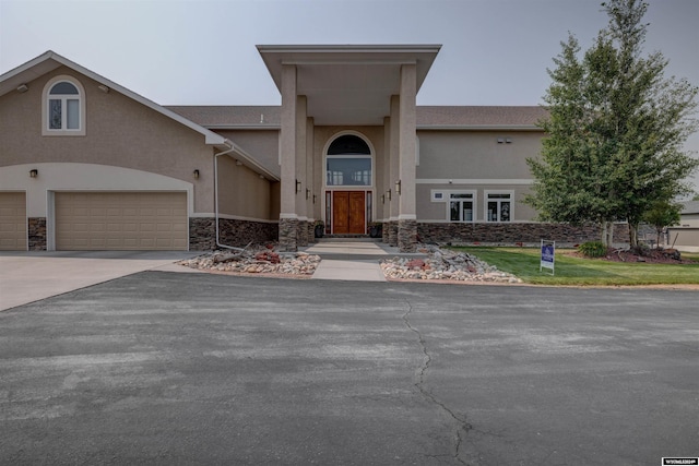 view of front facade with driveway, stone siding, and stucco siding