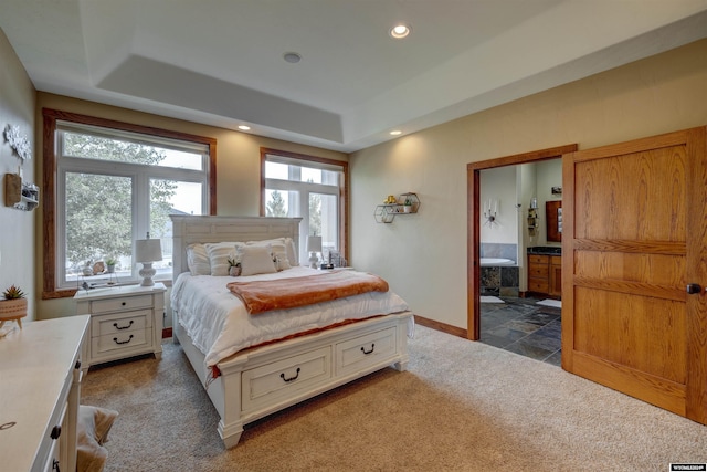 bedroom with a tray ceiling, dark colored carpet, recessed lighting, ensuite bath, and baseboards