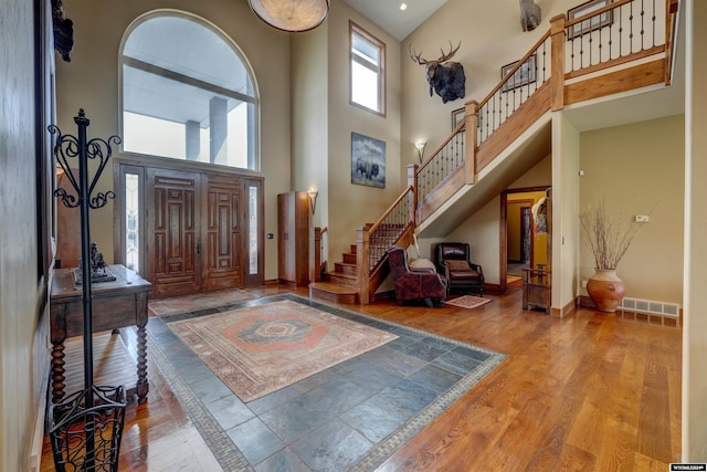 foyer featuring a high ceiling, wood finished floors, visible vents, baseboards, and stairs