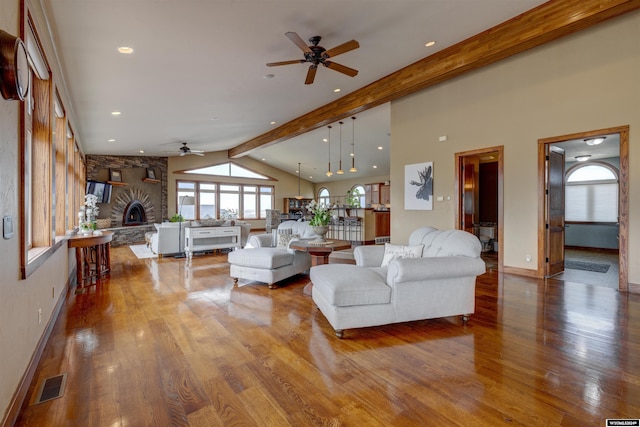 living room with baseboards, visible vents, wood finished floors, vaulted ceiling with beams, and a stone fireplace