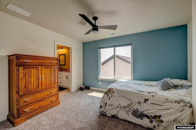 carpeted bedroom with baseboards, visible vents, ensuite bathroom, and a textured ceiling