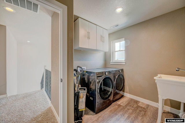 clothes washing area featuring a textured ceiling, light wood-style floors, visible vents, and washing machine and clothes dryer