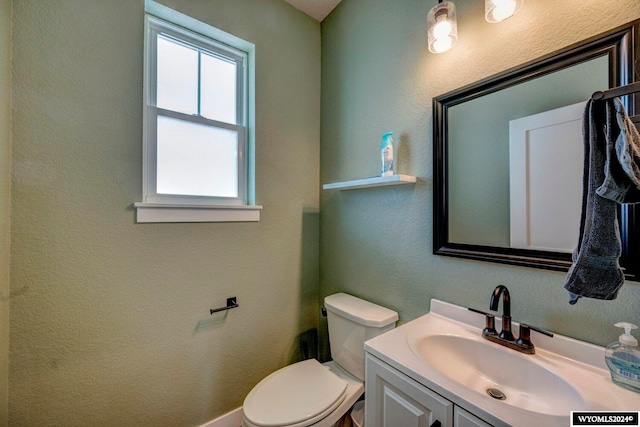 half bathroom featuring toilet, vanity, and a textured wall