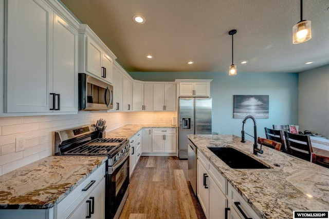 kitchen featuring light wood-type flooring, pendant lighting, a sink, appliances with stainless steel finishes, and light stone countertops