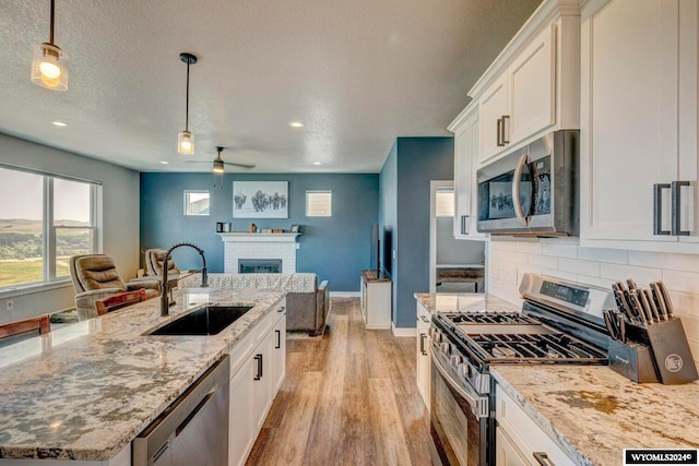 kitchen with a brick fireplace, open floor plan, appliances with stainless steel finishes, light wood-style floors, and a sink