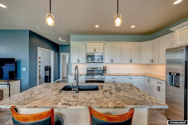 kitchen featuring tasteful backsplash, appliances with stainless steel finishes, hanging light fixtures, white cabinetry, and a sink