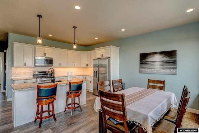 kitchen featuring decorative backsplash, wood finished floors, white cabinets, stainless steel appliances, and a sink