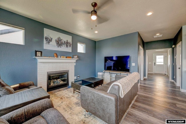 living area featuring wood finished floors, visible vents, baseboards, ceiling fan, and a brick fireplace