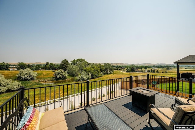 wooden terrace with a rural view, a lawn, and an outdoor fire pit