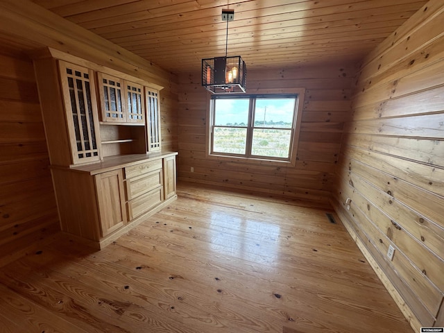 unfurnished dining area with light wood-type flooring, wood ceiling, wooden walls, and visible vents