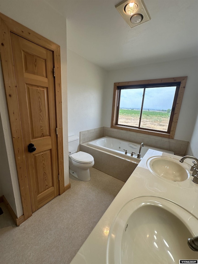 bathroom with double vanity, tiled bath, a sink, and toilet