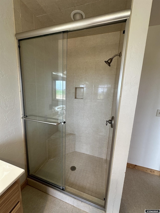 full bathroom with a stall shower, baseboards, a textured wall, and vanity