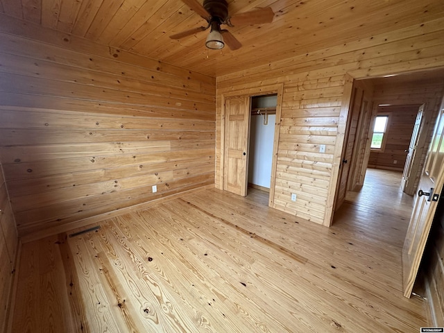 empty room featuring wood ceiling, wood walls, light wood-style flooring, and a ceiling fan