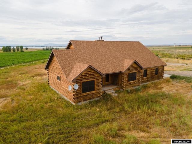 log-style house with a rural view, log exterior, roof with shingles, and a chimney