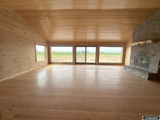 unfurnished living room with wooden ceiling, wood walls, wood finished floors, and a stone fireplace