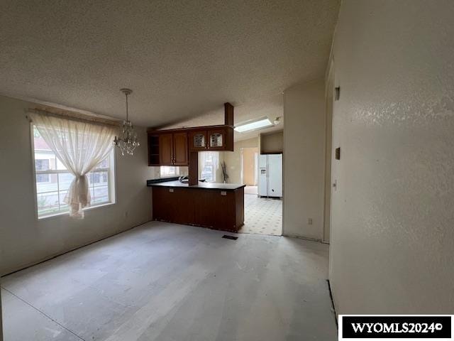 kitchen with an inviting chandelier, white refrigerator with ice dispenser, a textured ceiling, decorative light fixtures, and kitchen peninsula