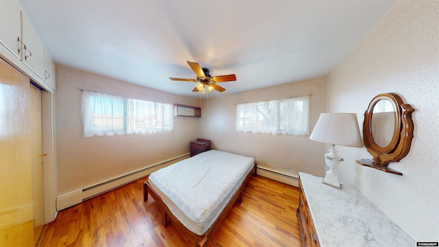 bedroom with light hardwood / wood-style floors, baseboard heating, a closet, and ceiling fan