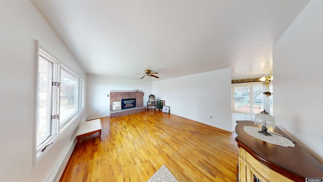 living room featuring light hardwood / wood-style floors, a baseboard heating unit, a fireplace, and ceiling fan