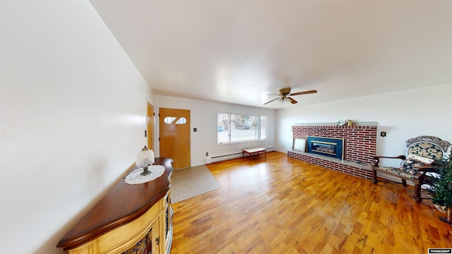 living room featuring light hardwood / wood-style floors, baseboard heating, a brick fireplace, and ceiling fan