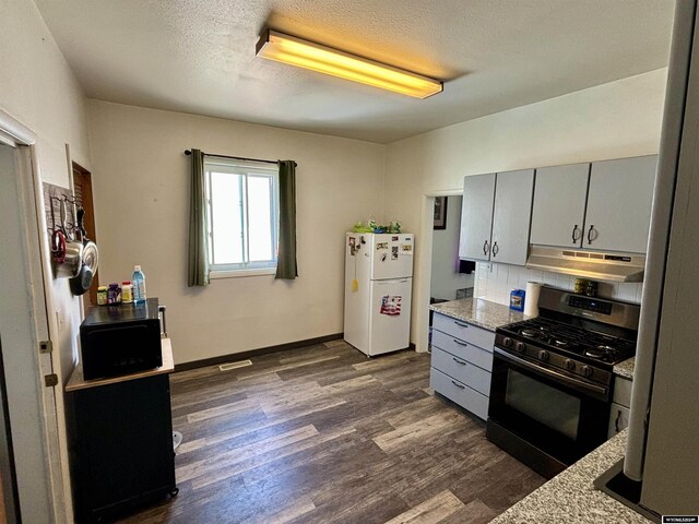 kitchen with dark wood-type flooring, white refrigerator, gas range, and light stone counters