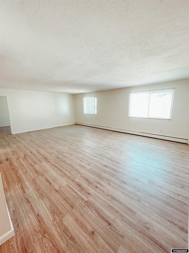 spare room with a textured ceiling, light wood-type flooring, and a healthy amount of sunlight