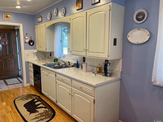 kitchen featuring light wood-type flooring, black dishwasher, sink, white cabinets, and decorative backsplash