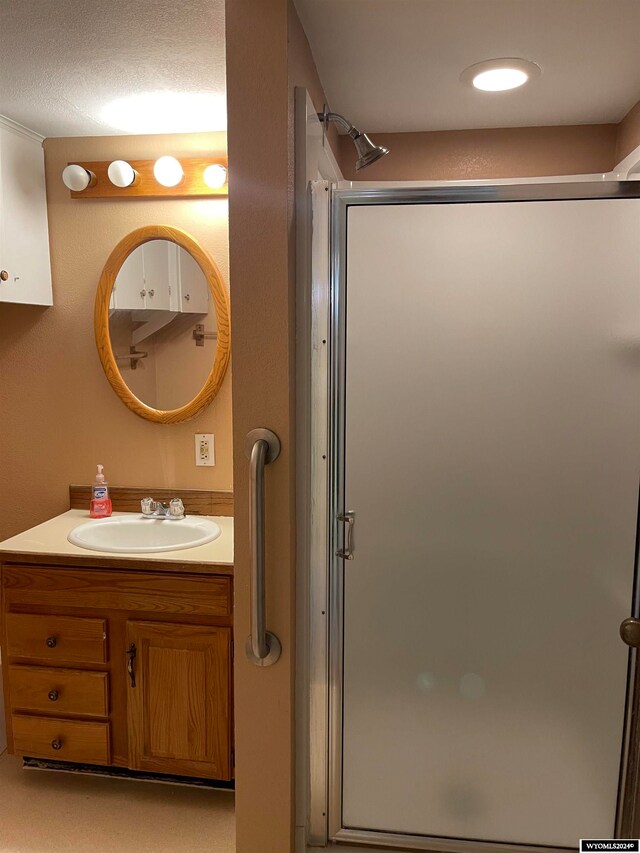 bathroom featuring a textured ceiling, vanity, and a shower with shower door