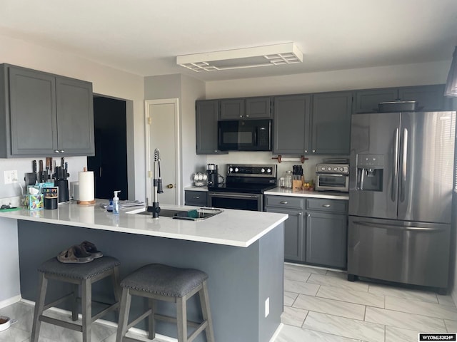 kitchen with sink, kitchen peninsula, gray cabinets, appliances with stainless steel finishes, and a breakfast bar area