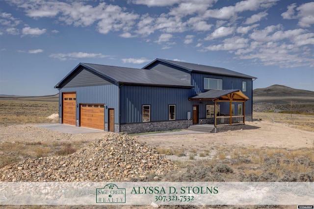 view of front facade with driveway, stone siding, metal roof, an attached garage, and a mountain view