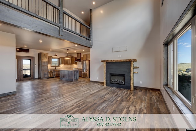 unfurnished living room with dark wood-style flooring, a fireplace, a towering ceiling, and baseboards