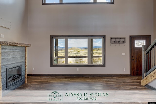 unfurnished living room with baseboards, a glass covered fireplace, stairway, wood finished floors, and a high ceiling