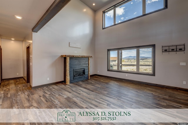 unfurnished living room with a glass covered fireplace, a high ceiling, baseboards, and wood finished floors