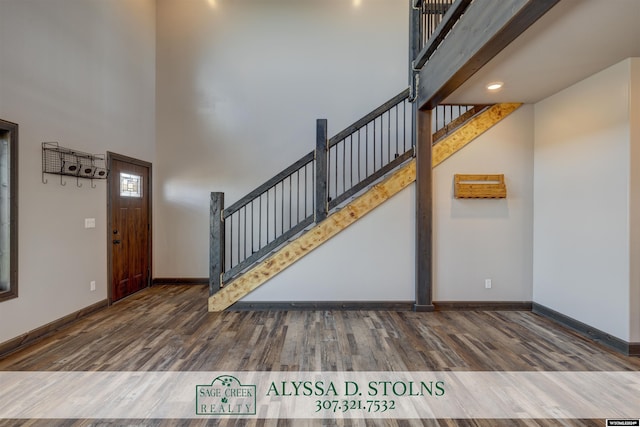 entrance foyer with stairs, a towering ceiling, baseboards, and wood finished floors