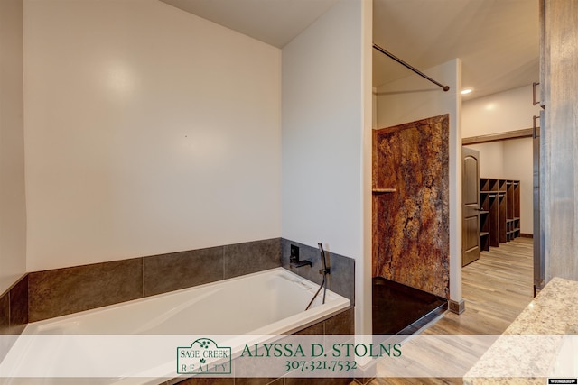 bathroom featuring walk in shower, wood finished floors, a bath, and a walk in closet