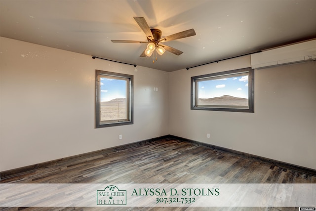 unfurnished room featuring ceiling fan, an AC wall unit, wood finished floors, and baseboards