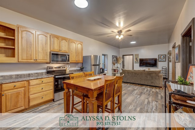 kitchen featuring a ceiling fan, appliances with stainless steel finishes, light brown cabinetry, light wood finished floors, and dark countertops