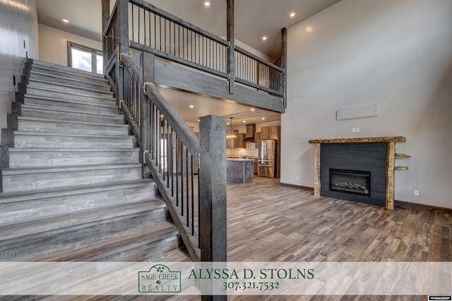 stairs featuring recessed lighting, a high ceiling, wood finished floors, baseboards, and a glass covered fireplace